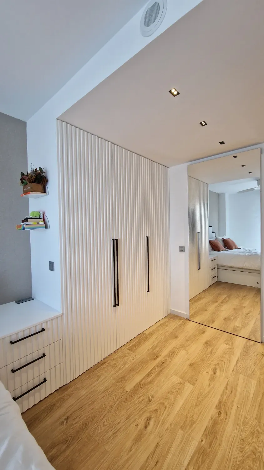 Un dormitorio con pisos de madera, gabinetes blancos y un espejo grande.