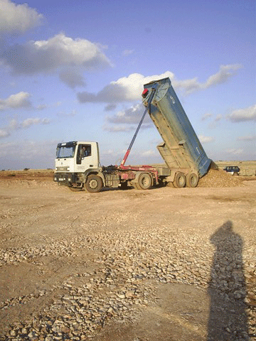 Un camión de volteo está estacionado en el medio de un campo de tierra.