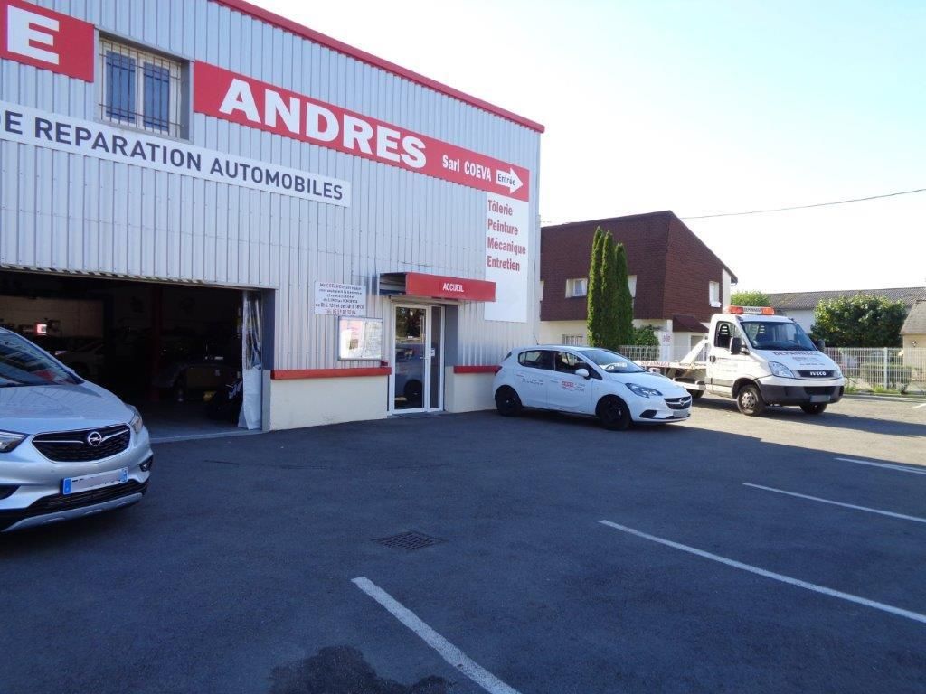 Extérieur d'un garage automobile avec une dépanneuse et des véhicules stationnés. Le garage présente des touches de rouge.