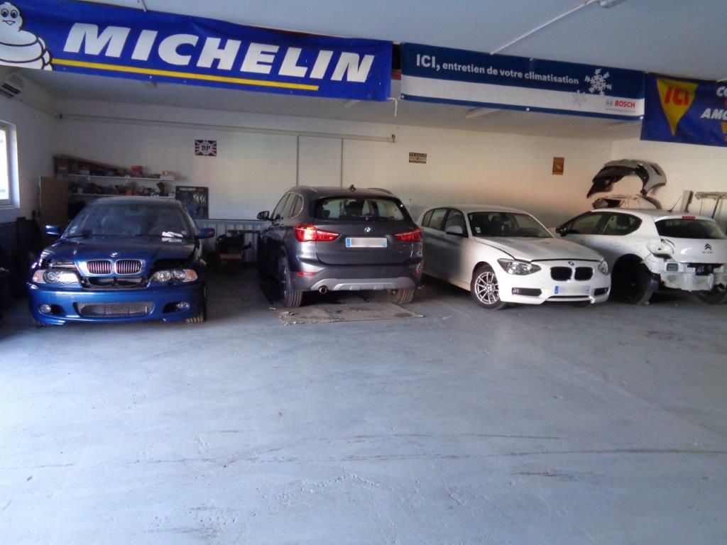 Voitures garées dans un garage ; véhicules bleus, gris et blancs sous un panneau Michelin.