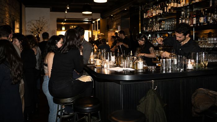 A crowded bar at night, guests packed along the counter under low amber light