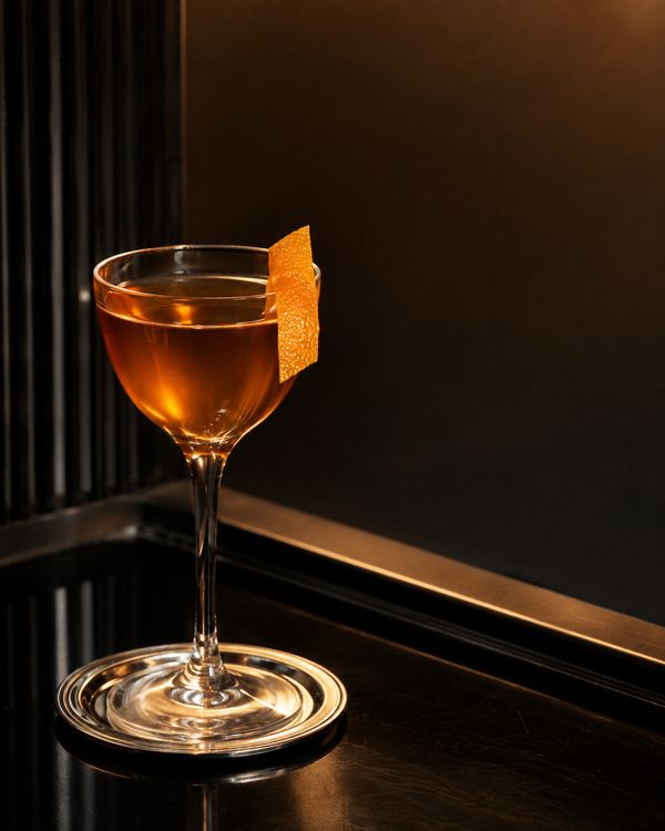 An amber cocktail with a burnt orange twist and a rosemary sprig in a rocks glass