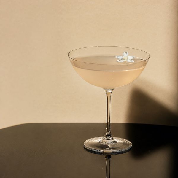 A pale, cloudy cocktail in a coupe glass garnished with a delicate flower