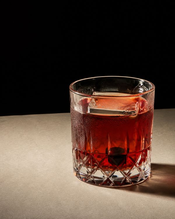 A deep red negroni over a single large ice cube in a rocks glass with an orange twist