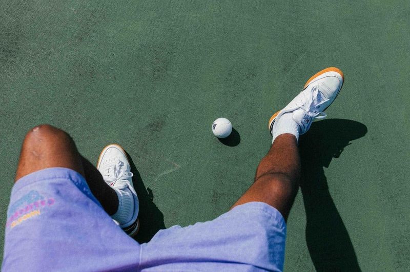 Sneakers and a yellow ball on a green padel court