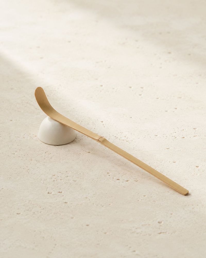 Bamboo and brass matcha scoop on a ceramic rest