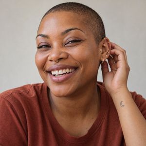 Lu Reyes, lead piercer, laughing with a curated ear and septum ring