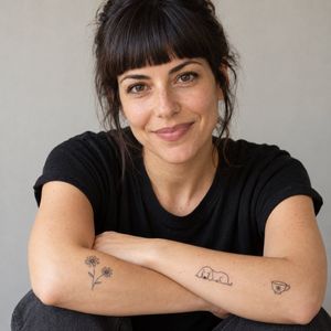 Noa Levin, tattoo artist, arms crossed showing tiny daisy and dog tattoos