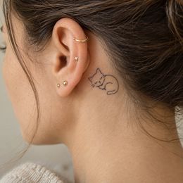 Curated ear of small gold piercings with a tiny sleeping-cat tattoo behind it