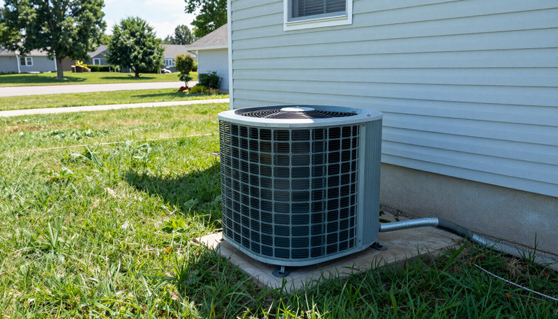 An outdoor air conditioner condenser beside a house on a bright summer day