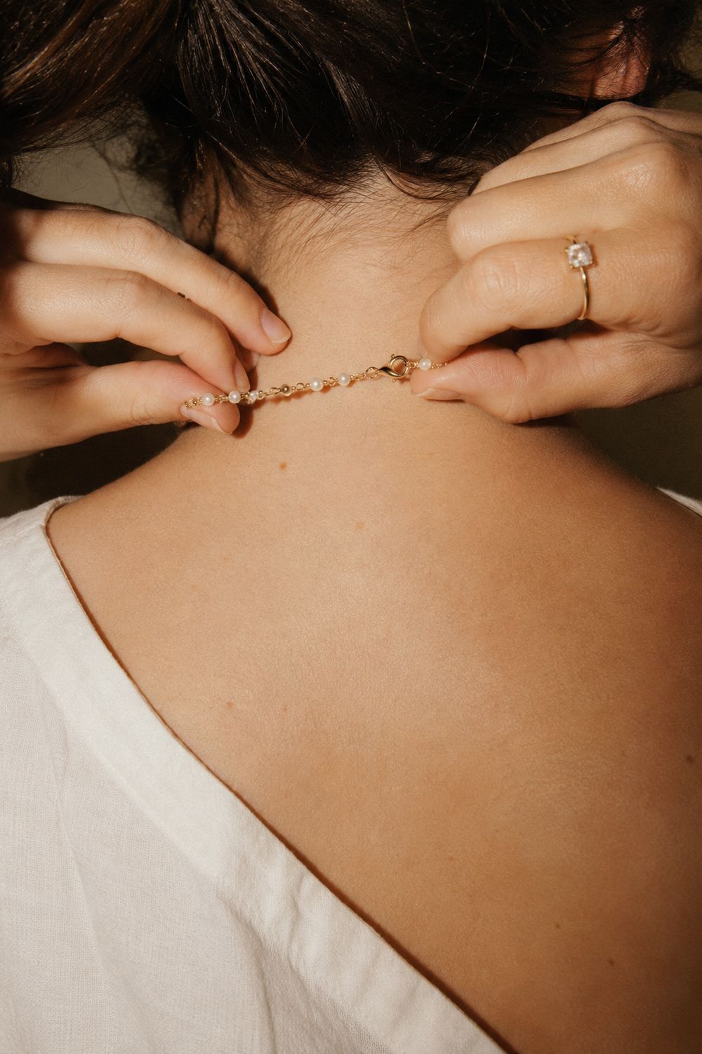 Close-up of a hand fastening the clasp of a Pearl gold necklace