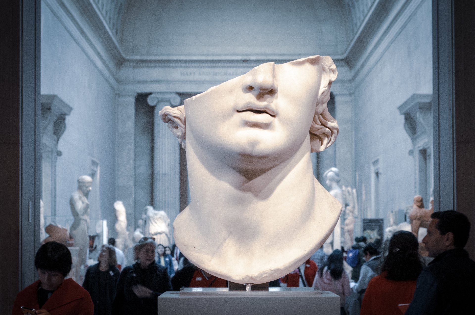 Eine Gruppe von Menschen betrachtet in einem Museum die Statue eines Männerkopfes.